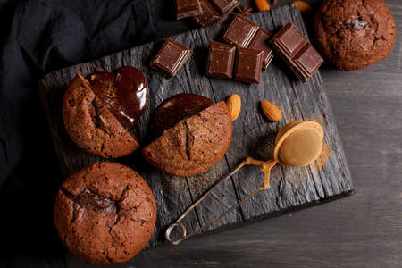 homemade muffins with chocolate, chocolate bars and almonds grains on a black wooden background. Cook prepares muffins with chocolate in the kitchen. Cook prepares muffins with chocolate in the bar.の写真素材