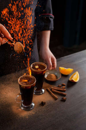 Preparation of mulled wine to serve, in a restaurant. Mulled wine in the preparation of the chef's bar. The hands of the chef on a dark black background. Burning mulled wine with sparks.の写真素材