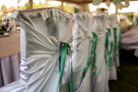 Decoration of chairs on a holiday. Chairs for the ceremony with a satin cape and green ribbon. stylish decorated chairs with ribbons at the reception in a restaurant for a wedding ceremonyの写真素材