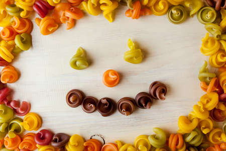 Colored pasta in the form of a spiral. Close-up of raw multi-colored rotini. Multicolored italian pasta, scattered on a white wooden background. Dry Italian pasta in five colors. Smiley. Smile pastaの写真素材