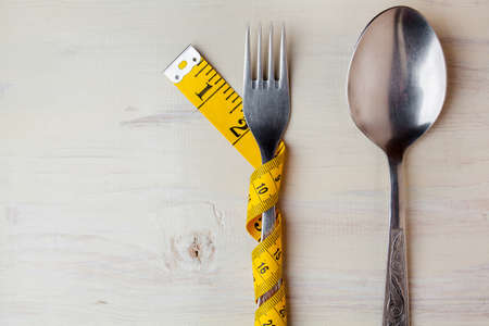 Diet, light wooden background, fork wrapped in a meter, fork and spoon on a white background, diet, meter, health concept, dietary background, diet concept, fork and spoon on a wooden backgroundの写真素材
