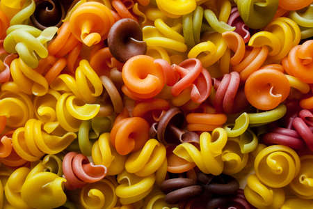 Colored pasta in the form of a spiral. Close-up of raw multi-colored rotini. Multicolored italian pasta, scattered on a white wooden background. Dry Italian pasta in five colors. space for textの写真素材