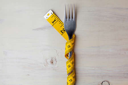 Diet, light wooden background, fork wrapped in a meter, fork and spoon on a white background, diet, meter, health concept, dietary background, diet concept, fork and spoon on a wooden backgroundの写真素材