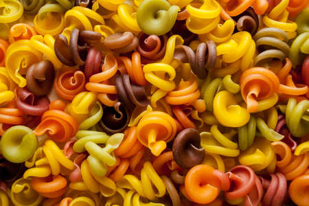 Colored pasta in the form of a spiral. Close-up of raw multi-colored rotini. Multicolored italian pasta, scattered on a white wooden background. Dry Italian pasta in five colors. space for textの写真素材