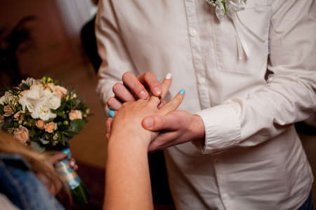 Newlyweds exchange rings, groom puts the ring on the bride's hand in marriage registry office. wedding rings and hands of bride and groom. young wedding couple at ceremony. matrimony.の写真素材