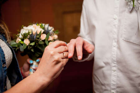 Newlyweds exchange rings, groom puts the ring on the bride's hand in marriage registry office. wedding rings and hands of bride and groom. young wedding couple at ceremony. matrimony.の写真素材