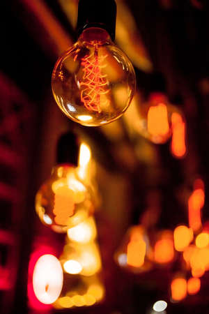Edison lamp on a black background. Incandescent lightbulb with a dark background with bokeh. Tungsten lamps it's make feeling to warm tone. Retro Edison light bulb with an unusual spiral, with bokehの写真素材