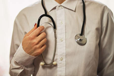 doctor with a stethoscope on hospital background. A doctor in a white coat with a stethoscope. treatment. A doctor in a white coat holds a stethoscope in his hands. Healthcare concept.の写真素材