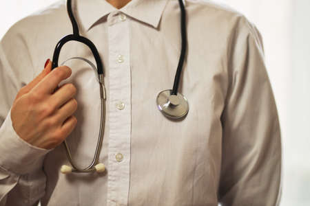 doctor with a stethoscope on hospital background. A doctor in a white coat with a stethoscope. treatment. A doctor in a white coat holds a stethoscope in his hands. Healthcare concept.の写真素材