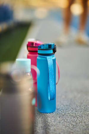 Close up blue and pink sports bottles stand on a blue rubber coated treadmill with a white line. Water sports drink on the background of a running track. blue and pink sports bottlesの写真素材