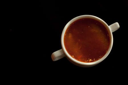 Red borscht in a white bowl isolated on a black background. Traditional Ukrainian beetroot soup with vegetables on a black table, on a black background.の写真素材