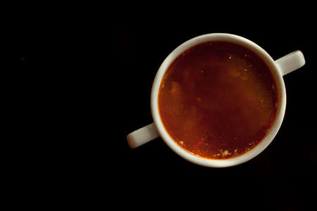 Red borscht in a white bowl isolated on a black background. Traditional Ukrainian beetroot soup with vegetables on a black table, on a black background.の写真素材