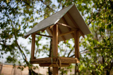 Wooden birdhouse on a background of foliage. Brown wooden birdhouse with foliage blurred in background. Square Wooden birdhouse on a tree.の写真素材