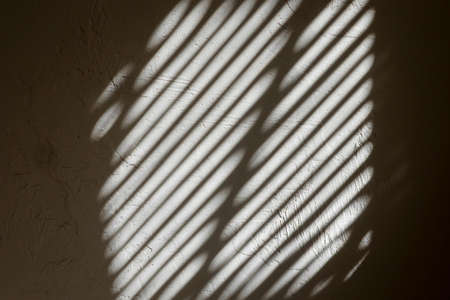 Shade from the blinds on the wall with plaster. Thin lines of light on the wall. The texture of the plaster. Shadow from the blinds. Place for your text.の写真素材