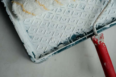 Roller with a red handle in a green pallet with white paint. Bucket with paint and a tray for paint and varnish. Roller and pallet with paint for rollers. Copy space for text. Concept of construction.の写真素材