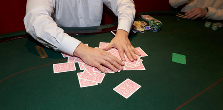 casino, gambling, poker, people and entertainment concept - close up of holdem dealer with playing cards and chips on green table. Male dealer at the casino at the table.の写真素材