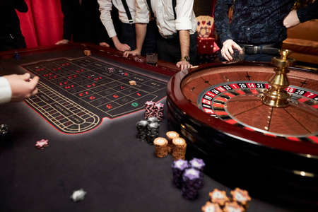 People play poker roulette at the table. Friends playing in the casino. A group of young people at a roulette table with a tape measure. Table for gambling in a luxury casino. Gambling Casino Rouletteの写真素材