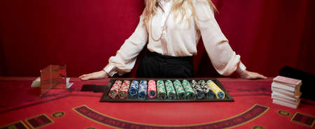 A croupier woman in a white shirt is standing at a red poker table. red Poker table in a luxury casino. Casino poker croupier womanの写真素材