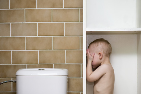 Boy standing in a bathroom cabinet covering his eyes with his hands with space for text or picture or product placement above and next to him.の写真素材