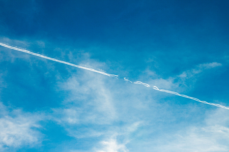 Single Interrupted chemtrail on azure sky with white clouds. Airplane trail. Curly trail. Chemtrail conspiracy theory.の写真素材