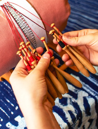 Making bobbin lace in traditional way. Detail on hands holding wooden bobbins with wound thread. Pillow lace.の写真素材