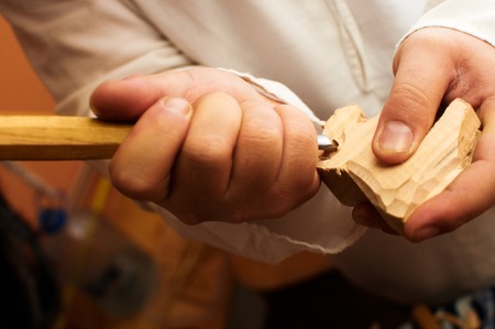Detail on man s hand holding a gouge, chisel and carving a sheep out of wood. Man in a white shirt making a wooden animal.の写真素材