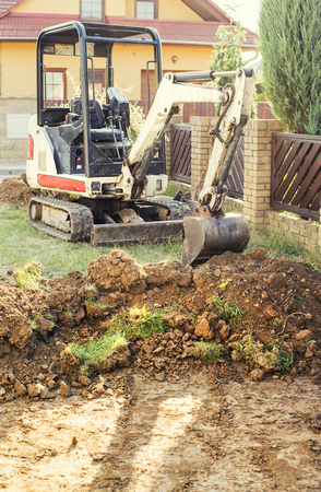 Mini excavator on construction site. Excavator regulates the terrain around the house. Digger digging soilの写真素材