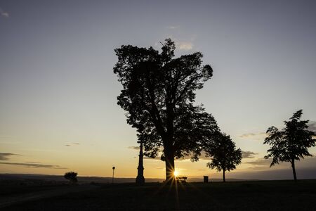 Tree silhouette in sunset with a wayside cross with field and road. Calvary in landscape. Olomouc Czech Republicの写真素材