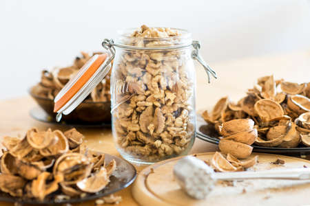 Large walnut kernels in a glass jar with plenty of empty cracked shells and a nutcrackerの写真素材