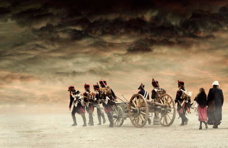 Napoleonic soldiers and women marching and pulling a cannon through plain land, empty countryside with stormy dark red clouds. No recognizable people.の写真素材