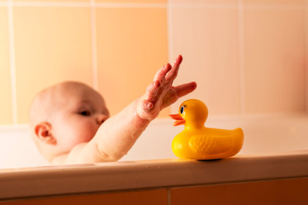 Brno Czech Rep 24-9-2014. Little boy sitting in a bath reaching out for a yelow plastic bathing...