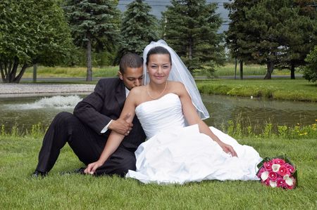 Just married multi ethnic couple sitting in the grassの写真素材