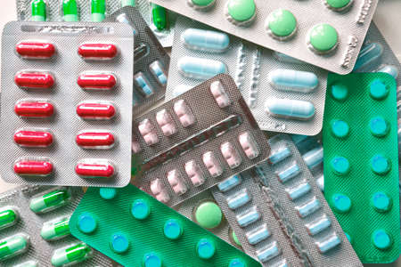 A pile of pills in blister packs. Blister packs full of multi-colored pills. Close-up on a light background. Full colored pills package. Pharmaceutical blister pack. Pack of pills with tablets.の写真素材