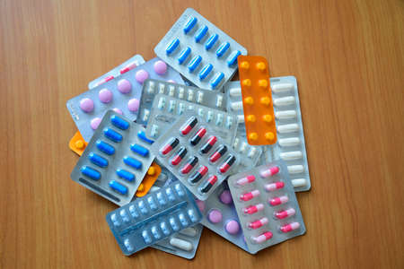 A pile of pills in blister packs. Blister packs full of multi-colored pills. Close up on wooden background. Full colored pills package. Pharmaceutical blister pack. Pack of pills with tablets.の写真素材