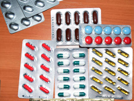 A pile of pills in blister packs. Blister packs full of multi-colored pills. Close-up on wooden background. Full colored pills package. Pharmaceutical blister pack. Pack of pills with tablets.の写真素材