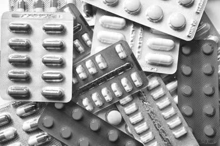 A pile of pills in blister packs. Close-up on a light background. Full colored pills package. Pharmaceutical blister pack. Pack of pills with tablets. Black and white photography.の写真素材