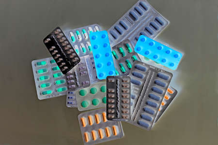A pile of pills in blister packs. Blister packs full of multi-colored pills. Close-up on a dark background. Full colored pills package. Pharmaceutical blister pack. Pack of pills with tabletsの写真素材