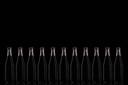 Eleven large glass bottles with a black drink stand on a mirrored surface against a dark background in the center.の写真素材