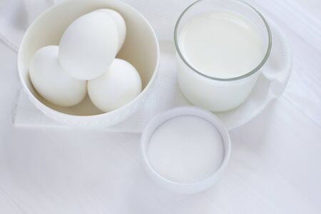 Four white eggs lie in a plate on a white wooden table next to a towel and a glass of milk and a salt shaker.の写真素材