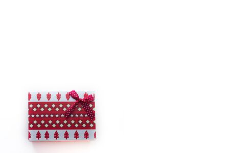 A red Christmas box with gifts and a bow stands on a white background with a place for a postcard text view from the top from the left edge. On the box are Christmas trees and snowflakes.の写真素材