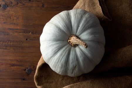 Still life of light pumpkin lies on a rough brown bag for vegetables on a wooden background view from the top close-up.の写真素材