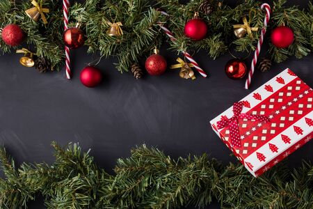 Coniferous Christmas garland decorated with red balls and golden bells with caramel canes at the top and bottom of the black table and a gift box with a bow in the corner.の写真素材