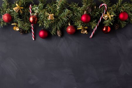 Coniferous Christmas garland decorated with red balls and golden bells with caramel canes at the top of the black table.の写真素材