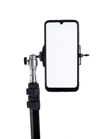 Smartphone mounted on a black tripod in a vertical position on a light isolated background tilted to the right.の写真素材