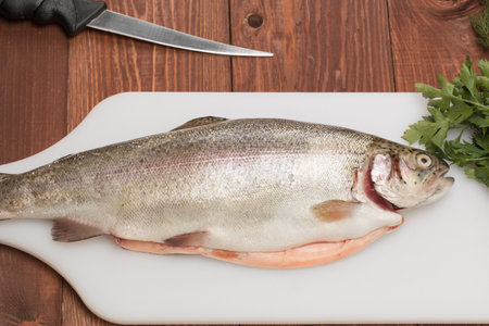 fresh trout fish on a cutting board with butter knife and spicesの写真素材
