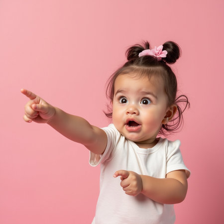 Surprised little girl pointing at copy space, isolated on pink backgroundの素材