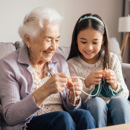 Smiling grandmother and granddaughter sitting on sofa and knitting together at homeの素材
