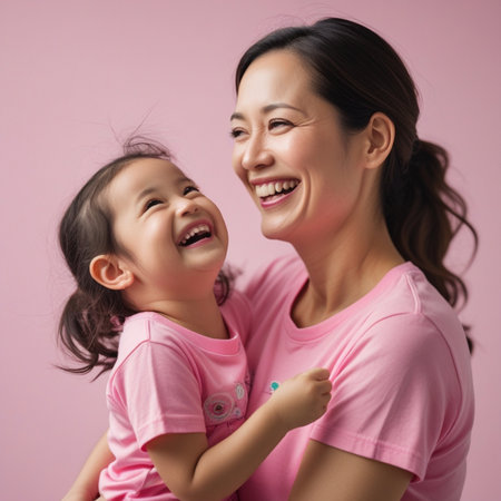 happy asian mother and daughter smiling at camera isolated on pink backgroundの素材