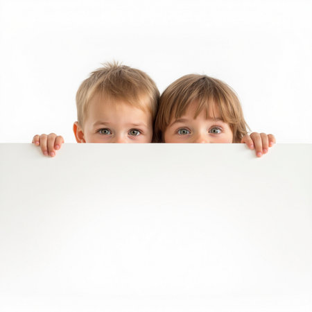 Two little girls hiding behind a white sheet of paper on a white backgroundの素材