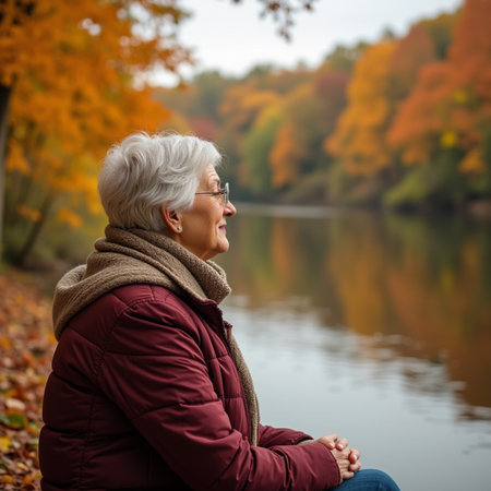Happy senior woman sitting on the bank of the lake in autumn parkの素材